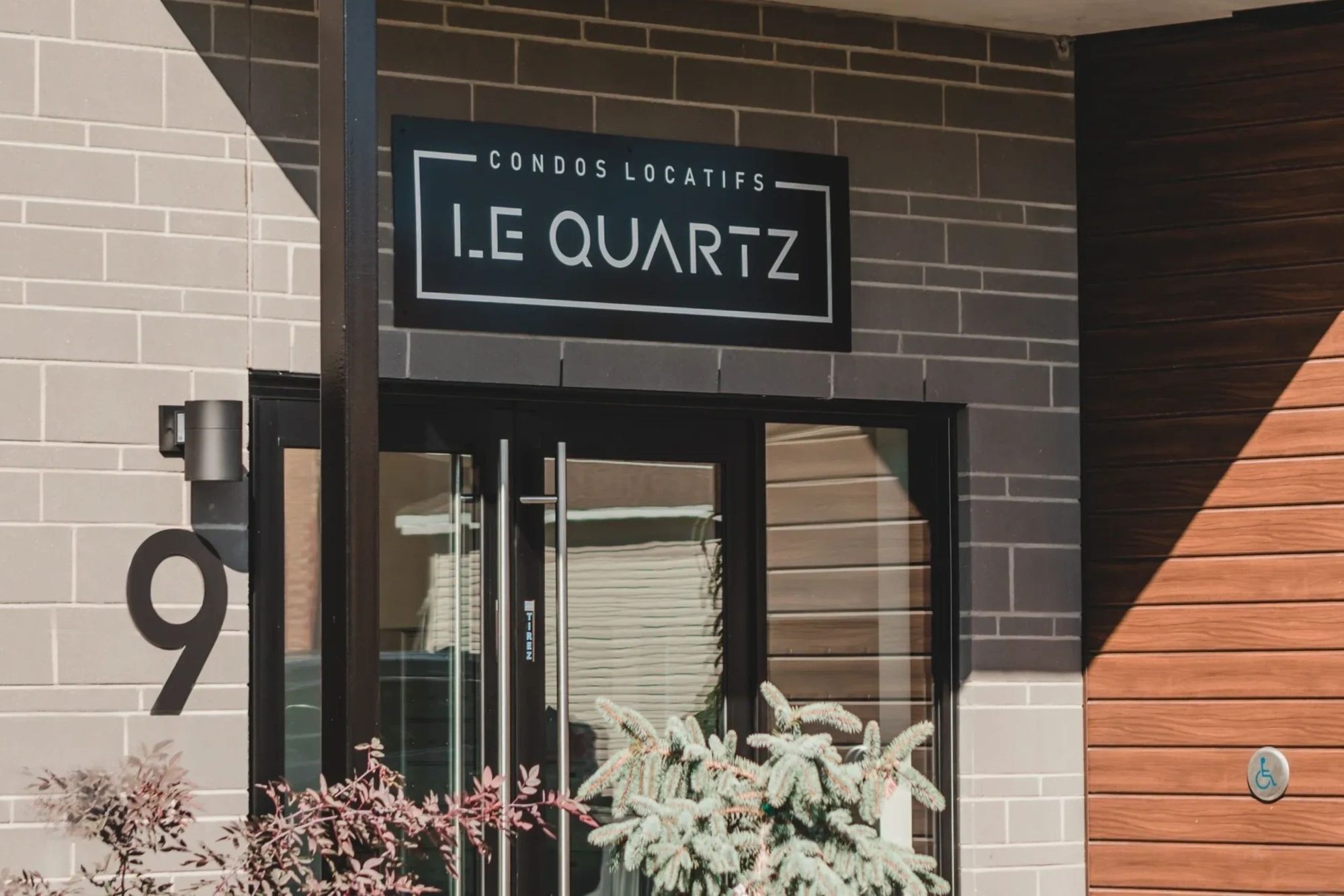 L'enseigne « Condos locatifs Le Quartz » et le numéro 9 sur le parement de pierre grise, à côté de l'entrée vitrée